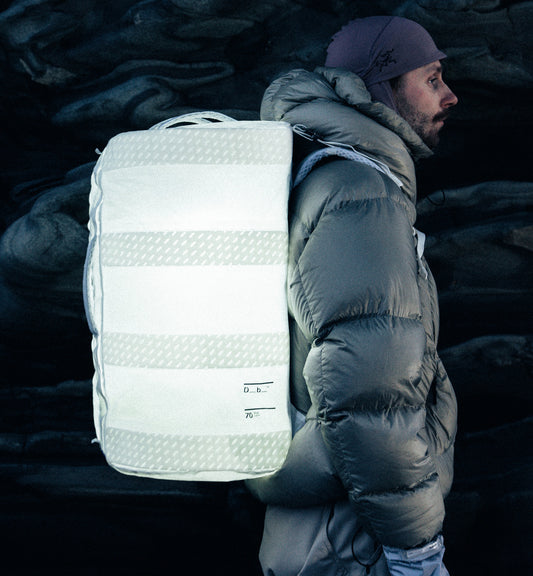Db Weigh Lighter Split Duffel 70Lを背負った旅行・スポーツシーンの使用イメージ。70Lの大容量ながら軽量で、アクティブな移動を快適にサポートします。色はAurora