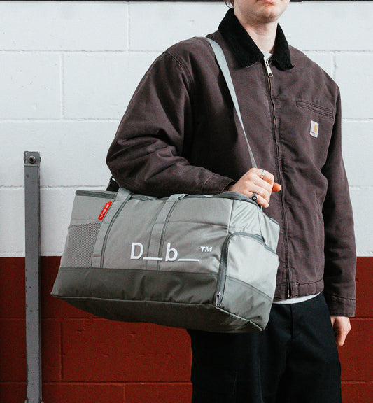 Dbのジムバッグ「Hauler Gym Bag 30L」の持ち歩きシーン。スポーツや旅行などアクティブなシーンに最適な、男女兼用のダッフルバッグです。色はBasil Green