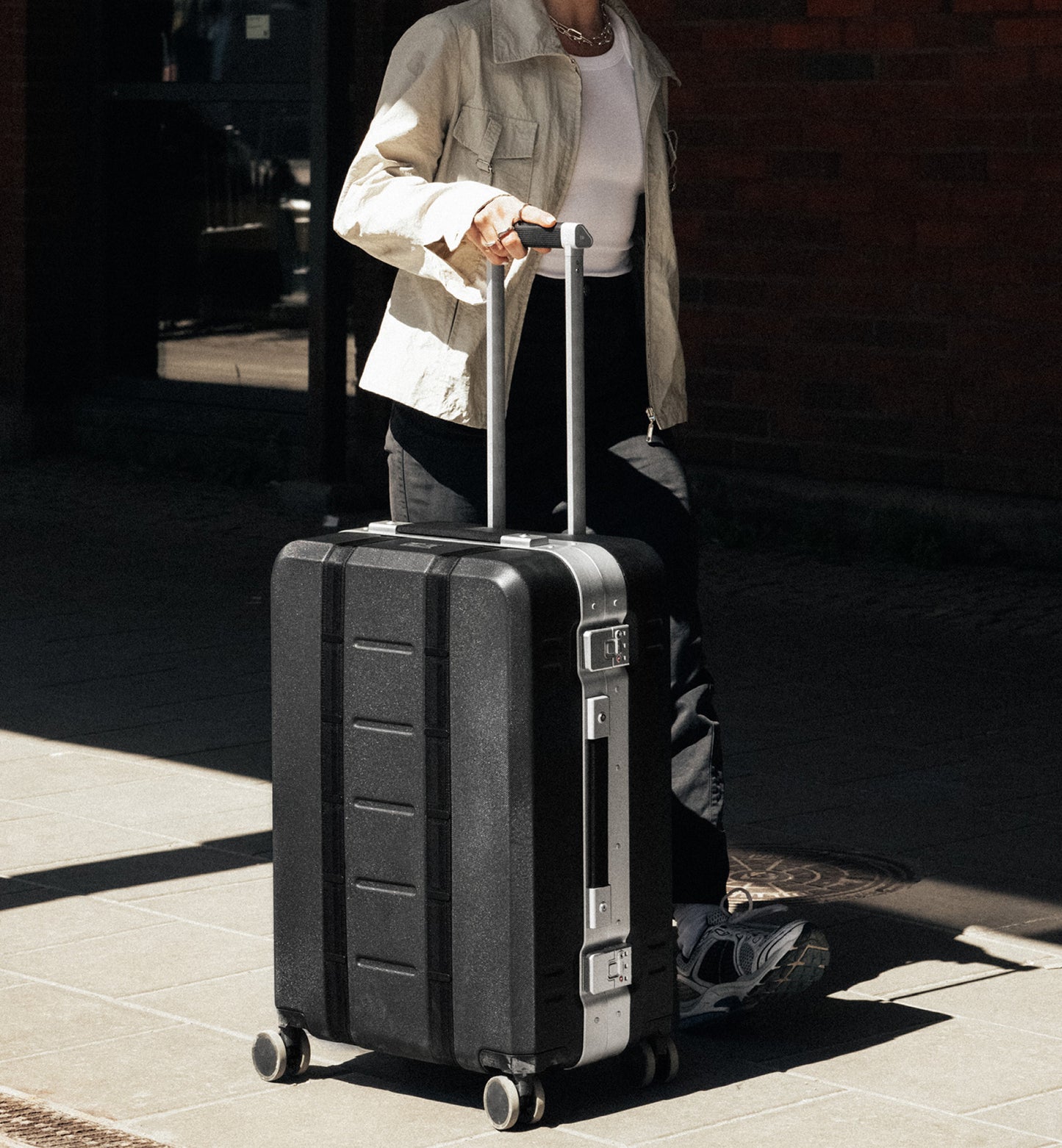 Dbの67L中型ハードスーツケース「Ramverk Pro Check-in Luggage Medium」のモデル使用画像。アクティブな旅やスポーツ遠征に最適な、耐久性の高いキャリーケースです。色はSilver
