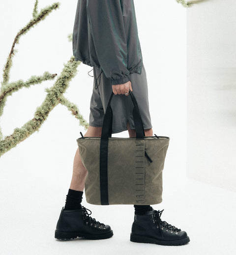 容量20リットルのトートバッグ、Db Essential Tote 20L の着用画像。旅好きやスポーツ好きの大人に向けた、シンプルでスポーティなデザインです。色はForest Green