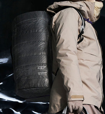 Db Weigh Lighter Split Duffel 70Lを背負った旅行・スポーツシーンの使用イメージ。70Lの大容量ながら軽量で、アクティブな移動を快適にサポートします。色はWeigh Darker