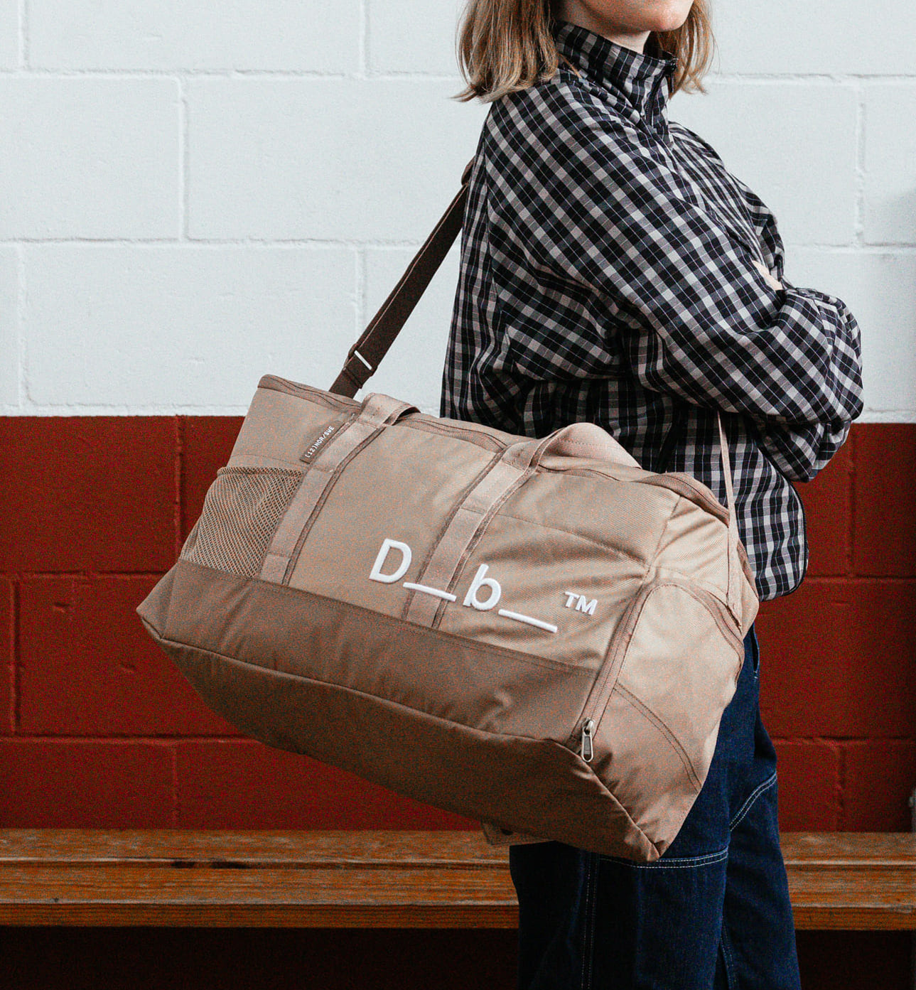 Dbのジムバッグ「Hauler Gym Bag 30L」の持ち歩きシーン。スポーツや旅行などアクティブなシーンに最適な、男女兼用のダッフルバッグです。色はAffogato Brown