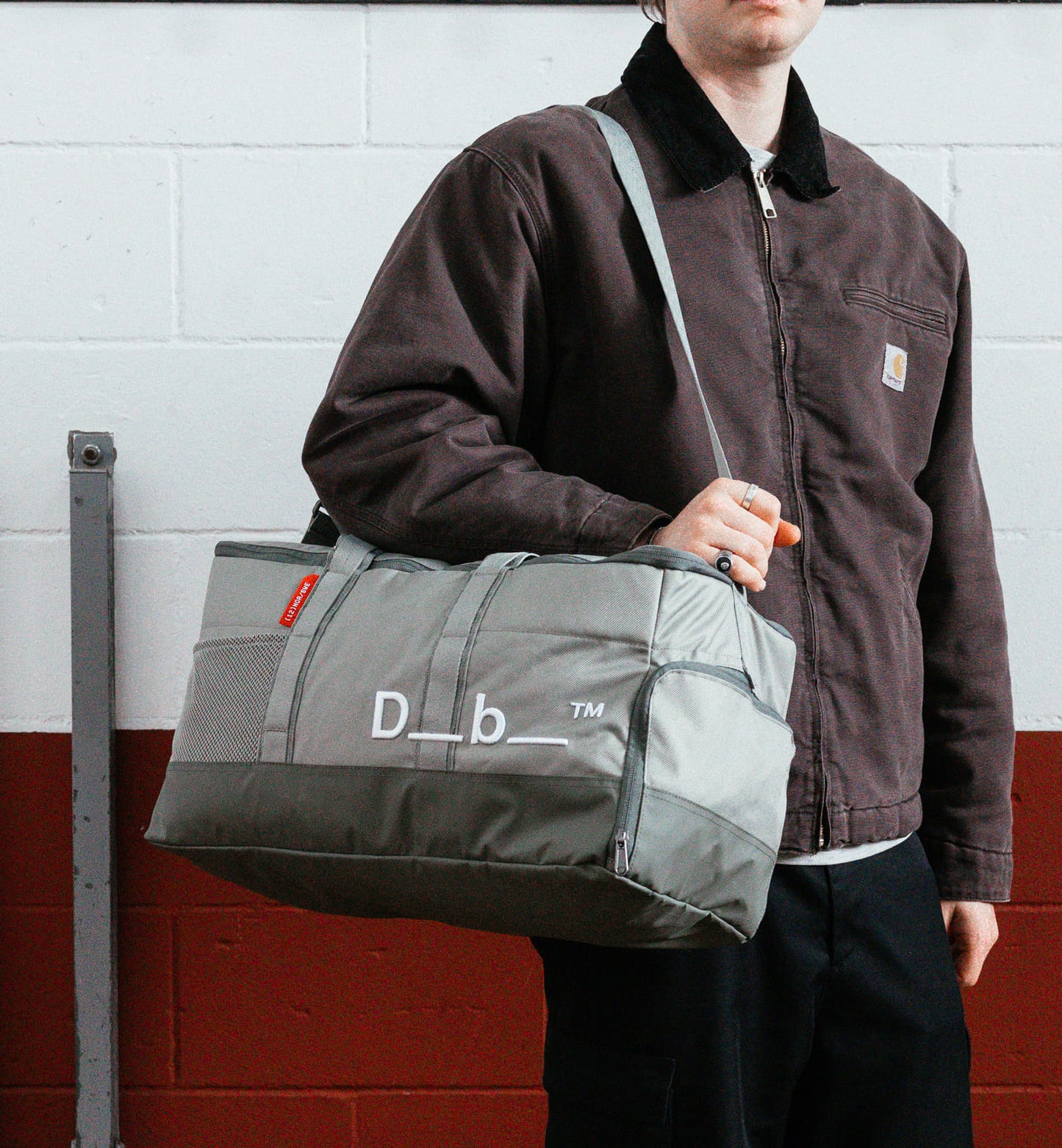 Dbのジムバッグ「Hauler Gym Bag 30L」の持ち歩きシーン。スポーツや旅行などアクティブなシーンに最適な、男女兼用のダッフルバッグです。色はBasil Green