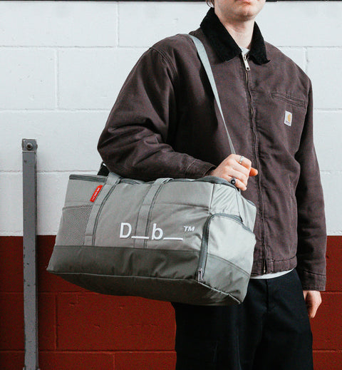 Dbのジムバッグ「Hauler Gym Bag 30L」の持ち歩きシーン。スポーツや旅行などアクティブなシーンに最適な、男女兼用のダッフルバッグです。色はBasil Green