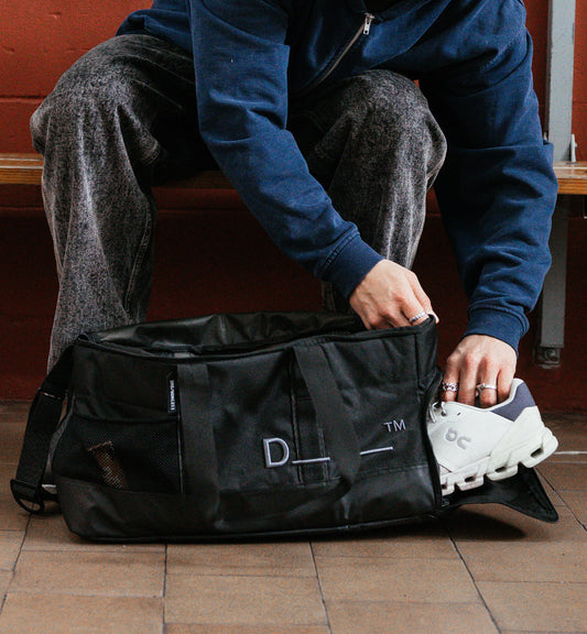 Dbのジムバッグ「Hauler Gym Bag 30L」のシューズ収納シーン。スポーツや旅行などアクティブなシーンに最適な、男女兼用のダッフルバッグです。色はBlack Out